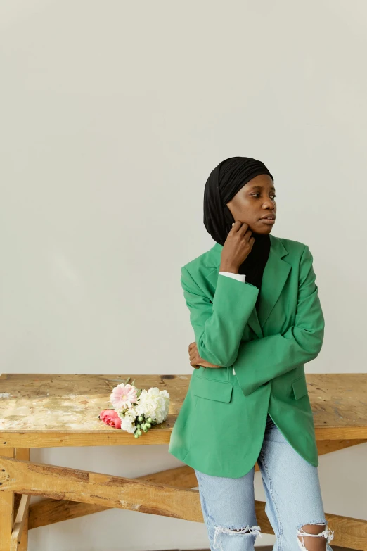 a woman sitting on a bench talking on a cell phone, an album cover, trending on pexels, wearing green suit, hijab, on a white table, arms folded