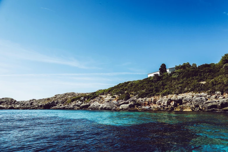 a white house sitting on top of a hill next to the ocean, a photo, inspired by Wilhelm Marstrand, unsplash, turquoise water, traditional corsican, thumbnail, clear blue skies