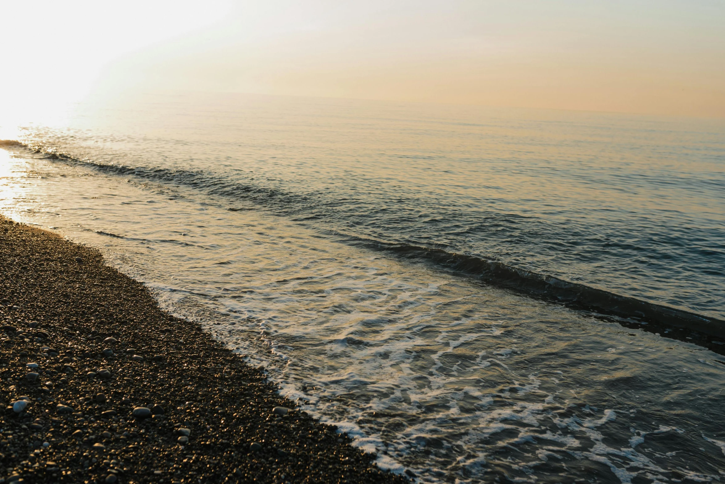 a man standing on top of a beach next to the ocean, by Carey Morris, pexels, romanticism, black sea, which shows a beach at sunset, rippling water, subtle detailing