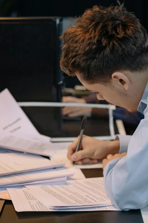 a man sitting at a desk writing on a piece of paper, for junior, cinematic, lachlan bailey, male teenager