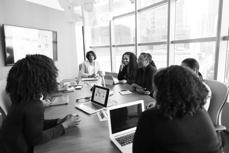 a group of people sitting around a table with laptops, a black and white photo, by Emma Andijewska, pexels, black female, presentation, overlooking, ad image