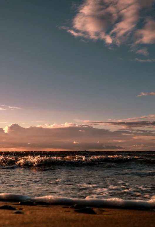 a man riding a surfboard on top of a sandy beach, during a sunset, viewed from the ocean, tumultuous sea, afar