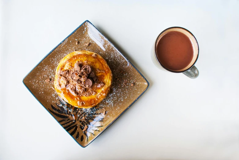 a plate topped with a pastry next to a cup of coffee, unsplash, sao paulo, pancakes, square, chocolate