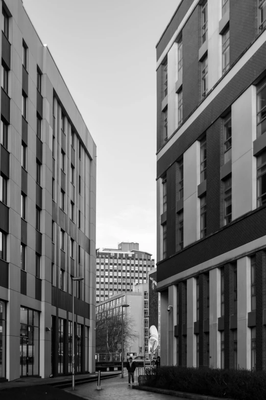 a black and white photo of a person walking down a street, inspired by Thomas Struth, unsplash contest winner, brutalism, glasgow in background, art deco office buildings, square, contrasting colours