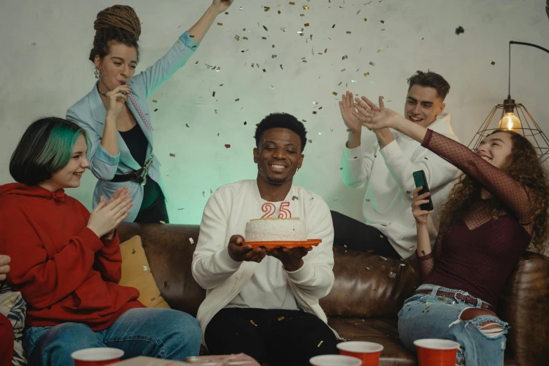 a group of people sitting on top of a couch, pexels, happening, birthday cake on the ground, black teenage boy, background image, video still