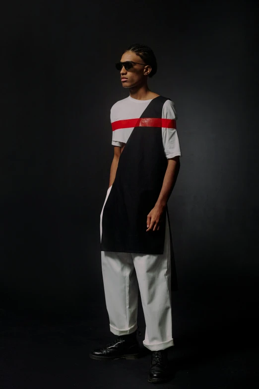 a man standing in front of a black background, inspired by Theo Constanté, suprematism, off - white collection, long tunic, left eye red stripe, black teenage boy