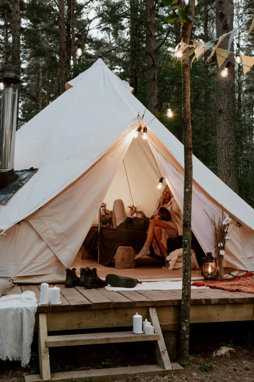 a couple of people sitting outside of a tent, floor lamps, finland, glamping, natural light outside