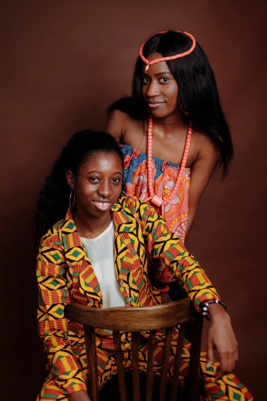 two women sitting next to each other on a chair, an album cover, by Chinwe Chukwuogo-Roy, headshot photograph, ( ( brown skin ) ), patterned clothing, 15081959 21121991 01012000 4k