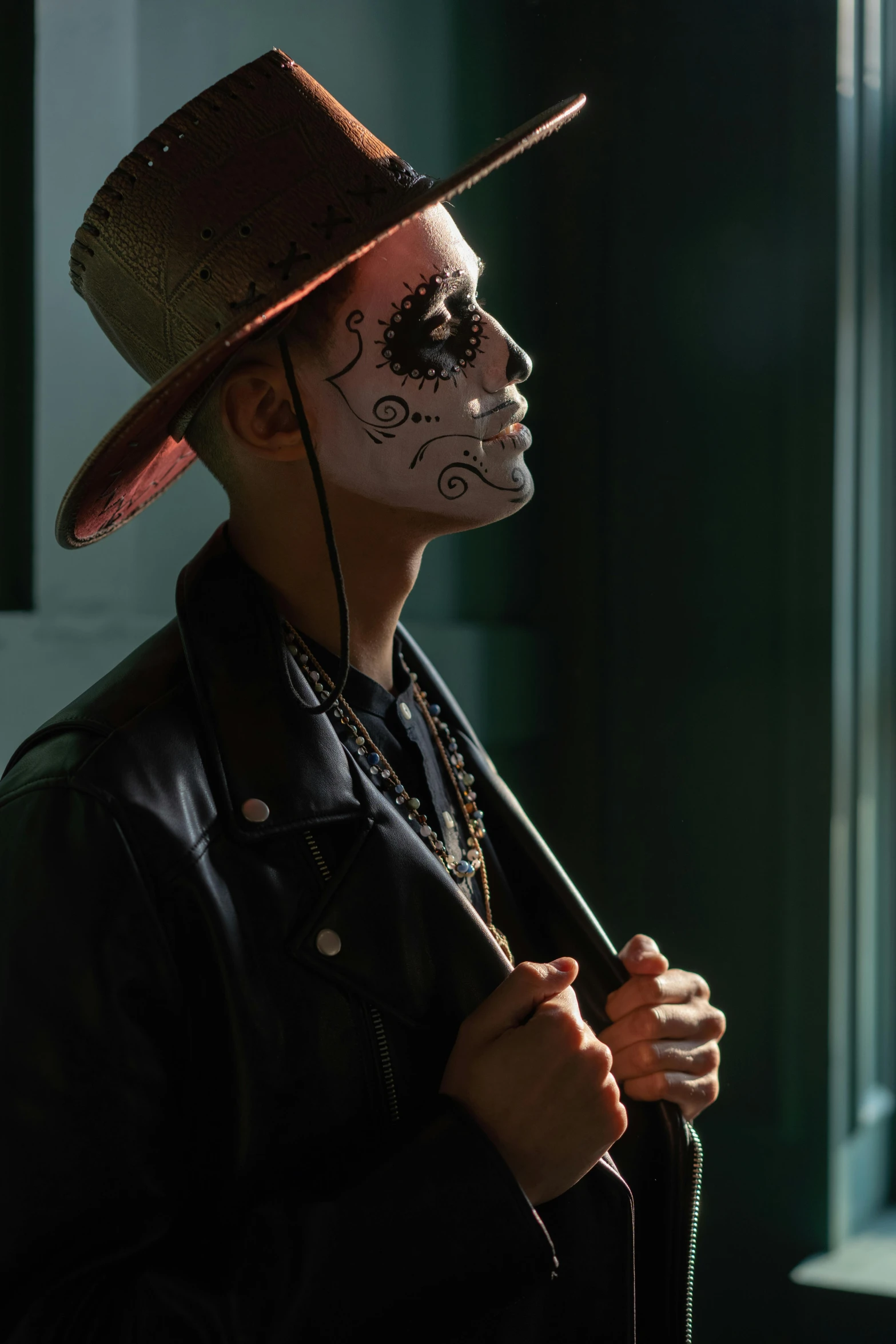 a man in day of the dead makeup holding an umbrella, by Elsa Bleda, pexels contest winner, wearing a bandana and chain, androgynous person, wearing a hat, in the shadows