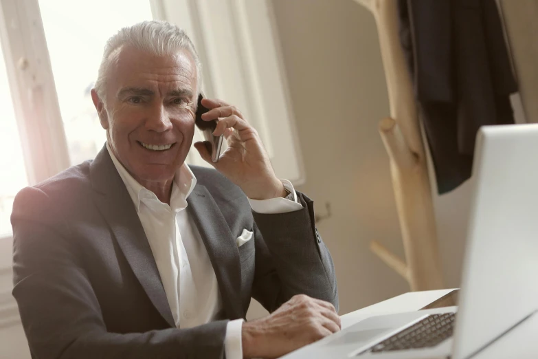 a man sitting in front of a laptop talking on a cell phone, dark grey haired man, tailored clothing, dean cornwall, thumbnail