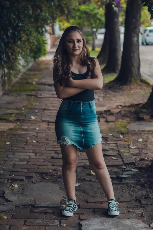 a woman standing on a sidewalk with her arms crossed, by Felipe Seade, pexels contest winner, wearing crop top and miniskirt, young southern woman, gif, mid 2 0's female