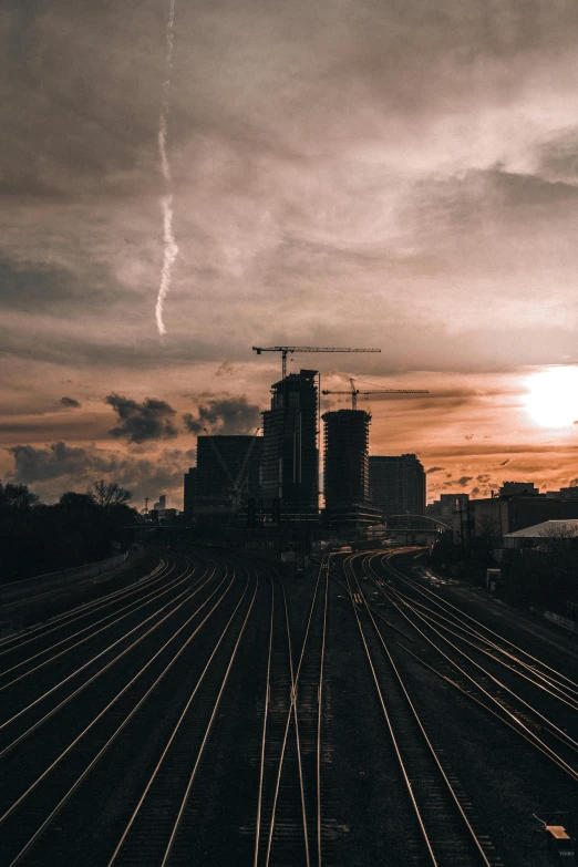 a train traveling down train tracks under a cloudy sky, a picture, pexels contest winner, high rise buildings, sun down, tall structures, streaks