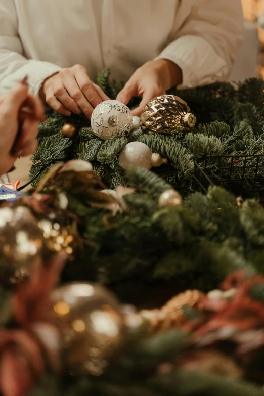 a woman decorating a christmas wreath with ornaments, by Jakob Gauermann, pexels contest winner, silver gold details, a cozy, trimmed, a handsome