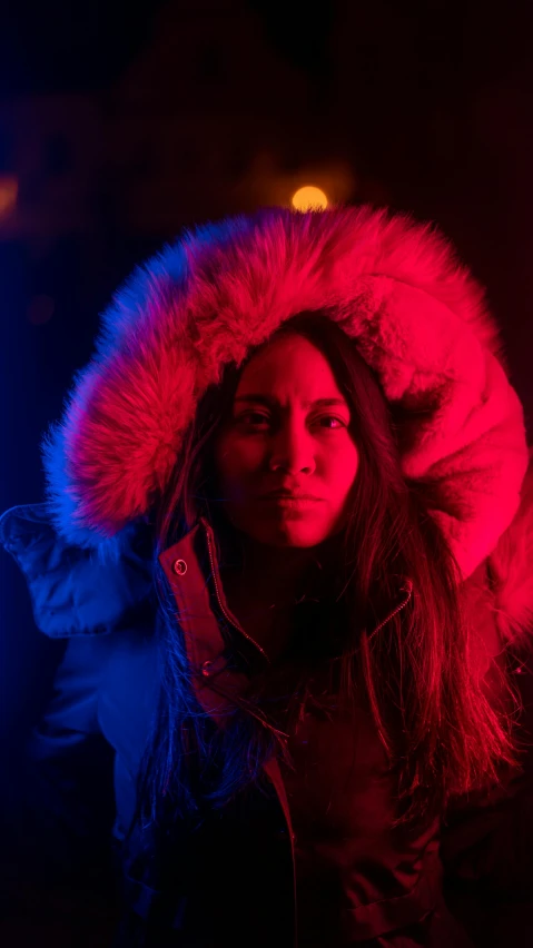 a woman standing in front of a red and blue light, an album cover, pexels, fur hood, inuit, intense look, sitting down