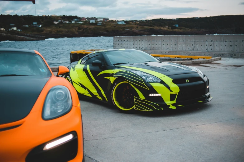 two cars parked next to each other near a body of water, by An Gyeon, pexels contest winner, yellow and black color scheme, samurai vinyl wrap, neon green lava streets, nissan gtr r 3 4