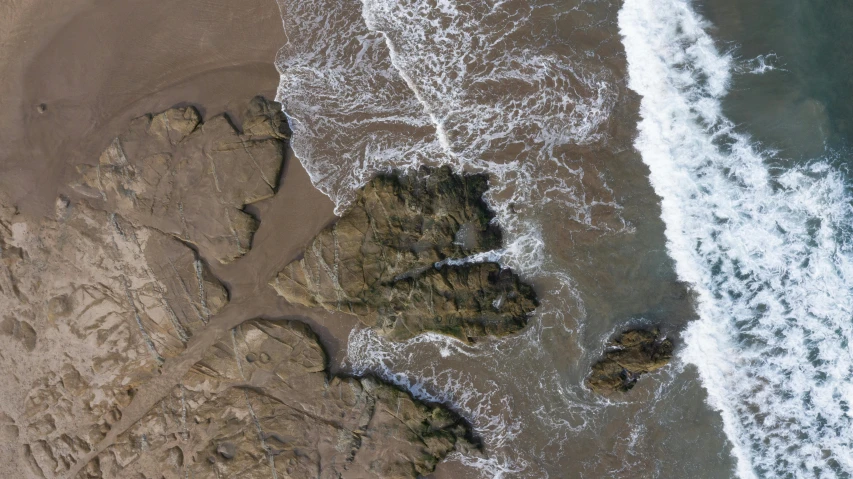 a couple of rocks sitting on top of a sandy beach, pexels contest winner, land art, high aerial shot, rivulets, california coast, rendered in houdini