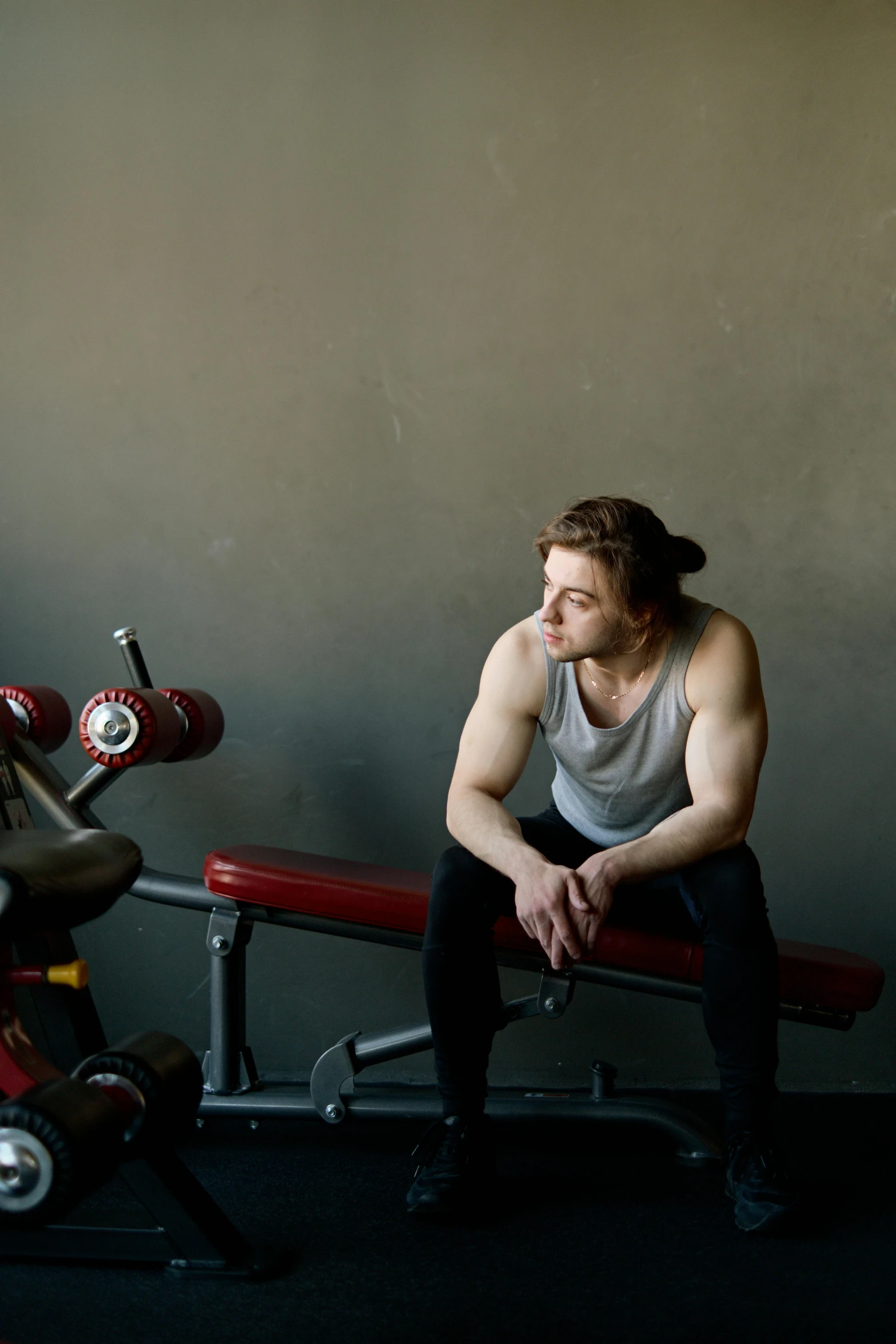 a man sitting on top of a bench next to a machine, wearing fitness gear, looking across the shoulder, lachlan bailey, promo image