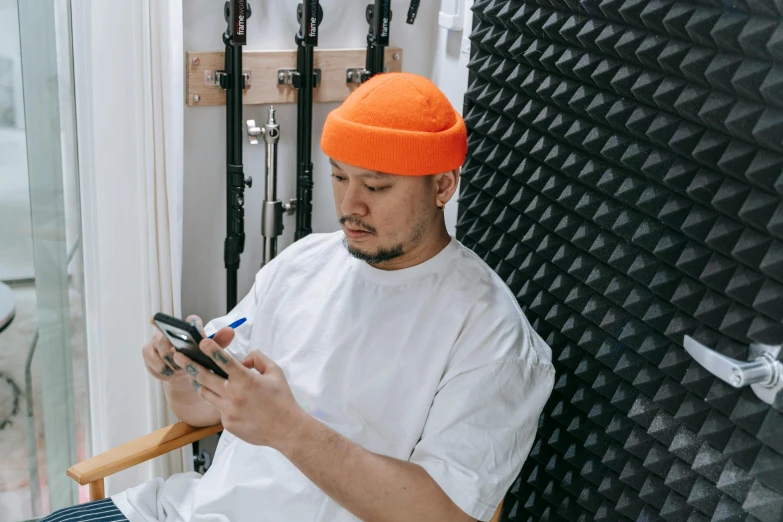 a man sitting in a chair holding a cell phone, trending on pexels, visual art, with rap cap on head, wearing an orange t-shirt, tomoyuki yamasaki, surgeon