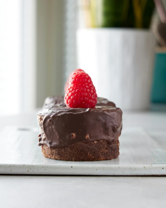 a piece of chocolate cake with a raspberry on top, a still life, inspired by Gordon Browne, unsplash, square, mini, ready-made, grey