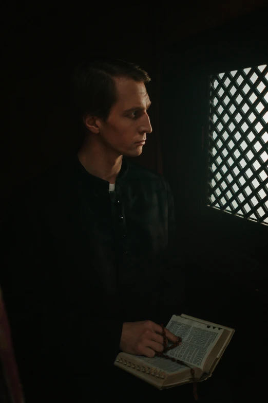 a man reading a book in front of a window, a colorized photo, inspired by Matthias Stom, unsplash, renaissance, sitting in a dark prison cell, steve buscemi, close-up portrait film still, vasnetsov