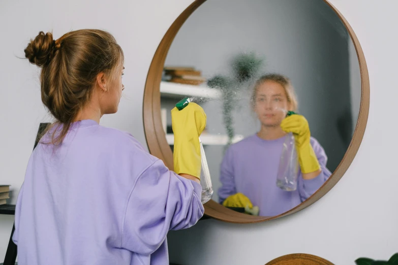 a woman in a purple shirt is cleaning a mirror, pexels contest winner, avatar image, low quality photo, clear image, profile image