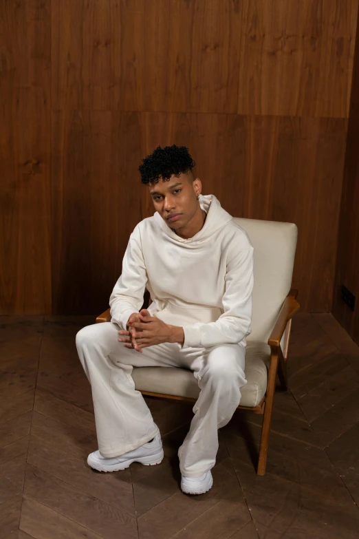 a man sitting on a chair in a room, an album cover, inspired by Louis Hersent, trending on pexels, renaissance, white outfit, black teenage boy, casual pose, ashteroth