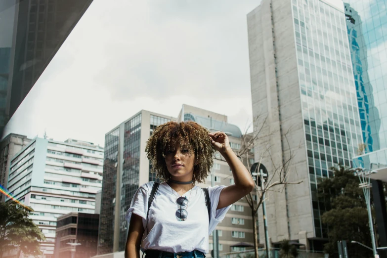 a woman standing in the middle of a city, a photo, by Emma Andijewska, pexels contest winner, afrofuturism, dressed in a white t shirt, hair is the focus, super cute funky black girl, white marble buildings