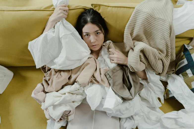 a woman laying on a couch covered in sheets of paper, inspired by Sarah Lucas, pexels contest winner, cozy calm! fabrics textiles, layered skirts, dua lipa, beige