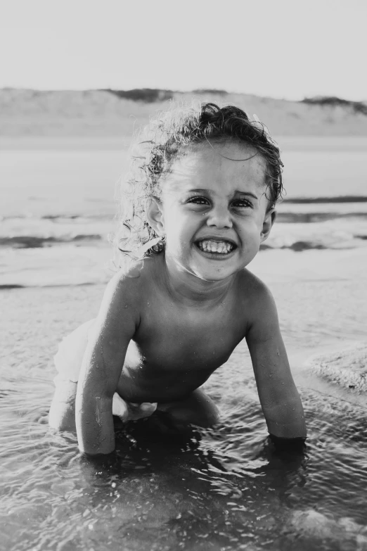 a black and white photo of a child on the beach, smiling seductively, made of water, curly haired, cheeky smile