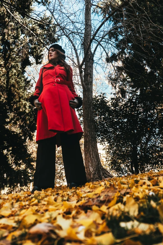 a woman in a red coat standing next to a tree, inspired by Evaline Ness, pexels contest winner, wide angle full body, fall season, bells, black