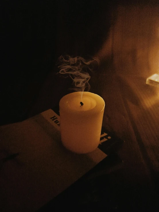 a lit candle sitting on top of a wooden table, an album cover, inspired by Elsa Bleda, unsplash, ignant, very smoky paris bar, low quality photo, yellow mist