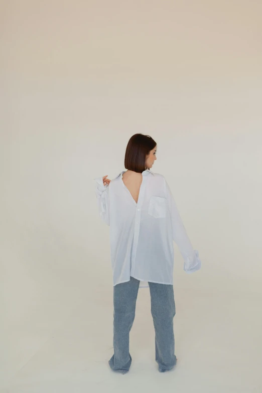 a woman standing in front of a white wall, an album cover, by Attila Meszlenyi, unsplash, long shirt, back view », translucent, baggy