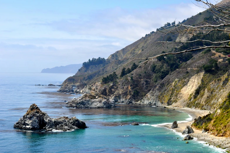 a large body of water next to a lush green hillside, by Carey Morris, pexels contest winner, california coast, maple syrup sea, tie-dye, clear blue water