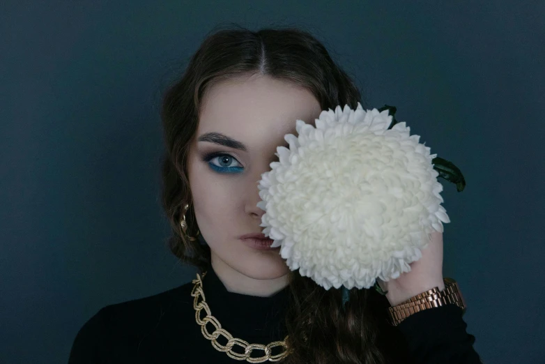 a woman holding a white flower in front of her face, an album cover, inspired by Elsa Bleda, aestheticism, holding gold watch, white + blue + gold + black, low quality photo, black eye makeup