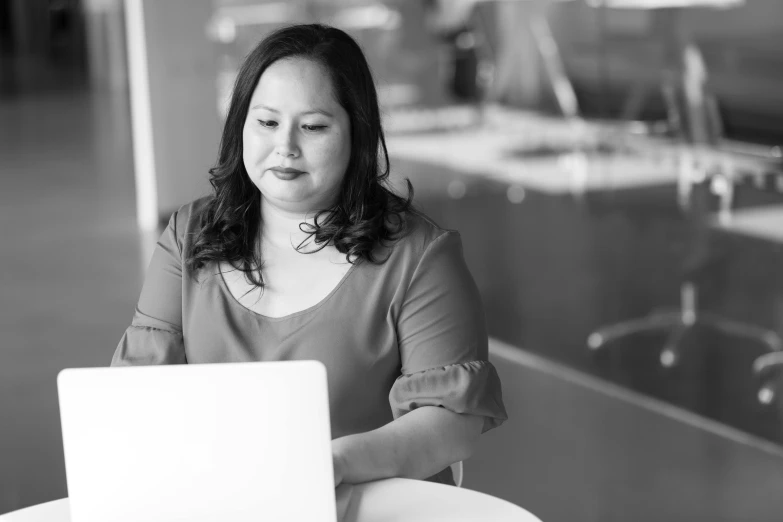 a woman sitting at a table with a laptop, a black and white photo, by Natasha Tan, plus size woman, cindy avelino, vp of marketing, joel torres