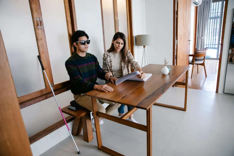 a couple of people sitting at a table with a laptop, unsplash, mingei, blind, no legs, indiecraft aesthetic, background image