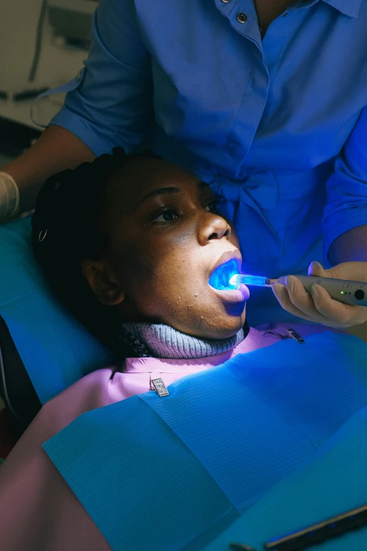 a woman sitting in a chair with a toothbrush in her mouth, pexels contest winner, happening, high blue lights, medical dissection, african american woman, uniform teeth