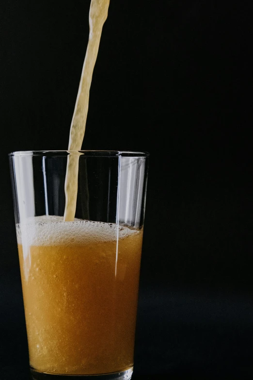 an orange juice being poured into a glass, by Tuvia Beeri, in front of a black background, promo image, freezing, new england ipa