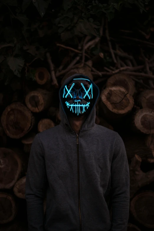 a man standing in front of a pile of logs, a hologram, pexels contest winner, graffiti, dark hooded wraith, glowing blue face, black mask, edm fans