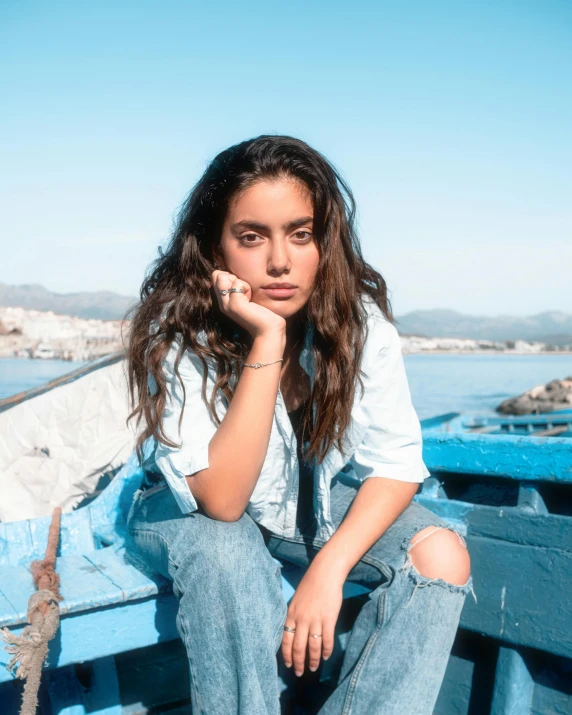 a beautiful young woman sitting on top of a blue boat, an album cover, by Olivia Peguero, trending on unsplash, happening, oona chaplin, baggy jeans, no makeup wavy hair, she is mexican