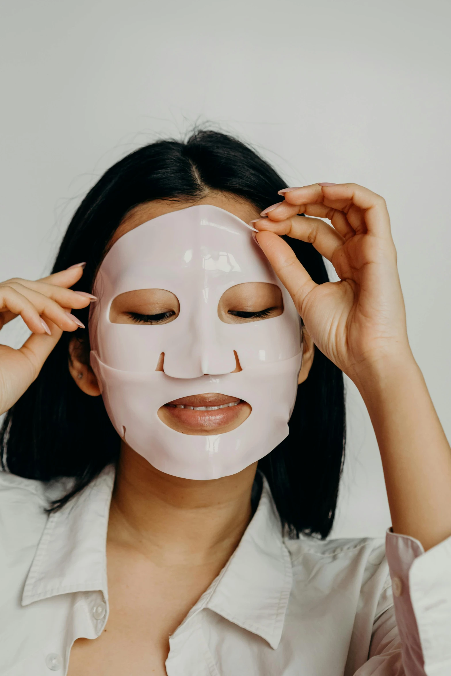 a woman putting a mask on her face, wide forehead, face and body clearly visible, silicone skin, asian features