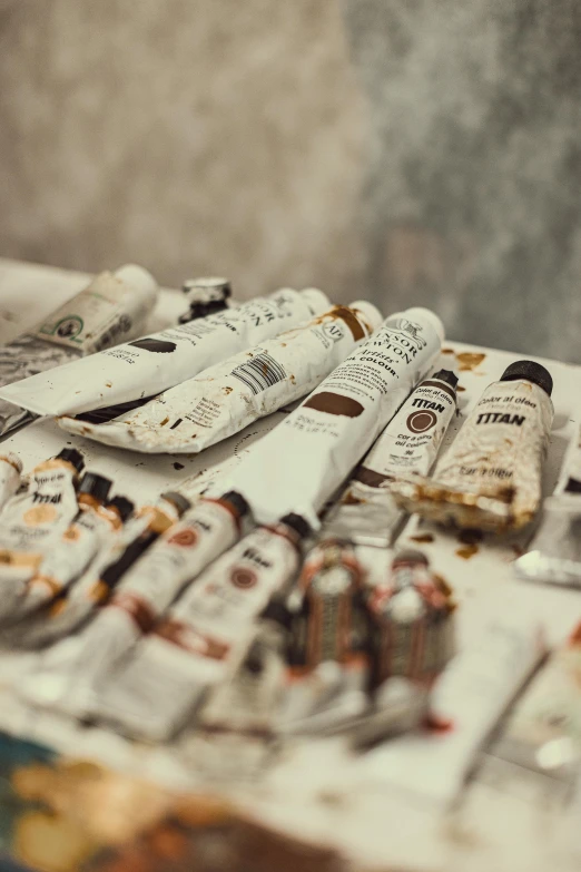 a bunch of paint brushes sitting on top of a table, inspired by Stanley Spencer, pexels contest winner, hyperrealism, light cream and white colors, paint tubes, brown, inside a grand messy studio