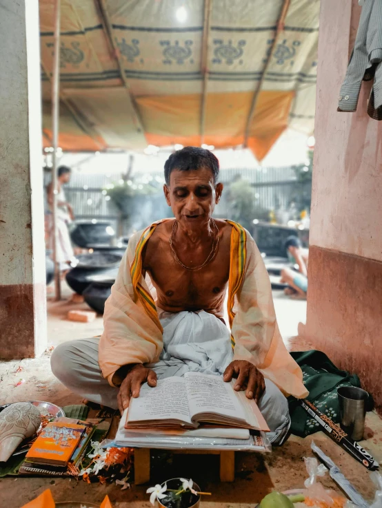 a man sitting on the ground reading a book, by Jan Tengnagel, pexels contest winner, bengal school of art, holy ceremony, portrait of a old, market, a still of a happy