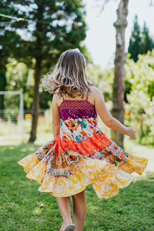 a little girl walking across a lush green field, swirly flower dress, patchwork-streak style, boho, vibrant and dynamic