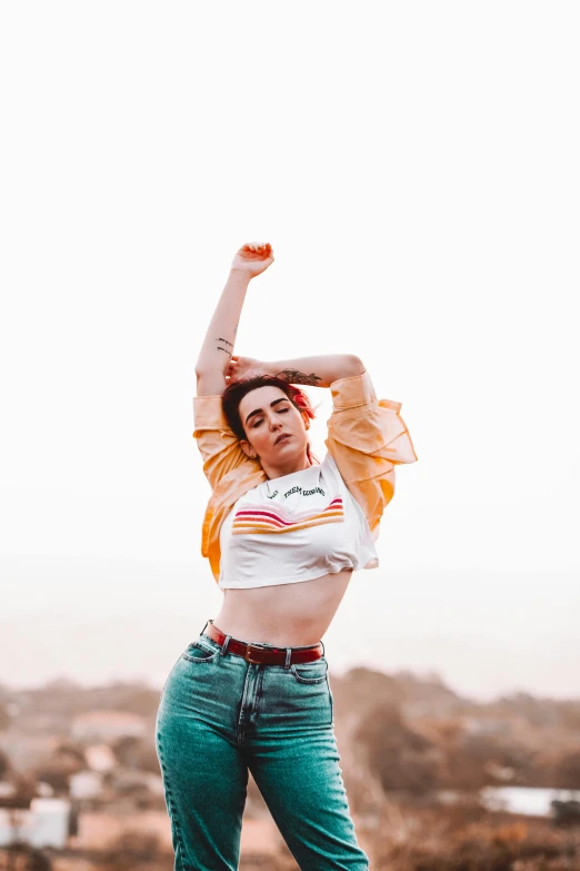 a woman jumping in the air with her arms in the air, an album cover, by Jessie Alexandra Dick, trending on pexels, non binary model, croptop, jeans and t shirt, fight pose