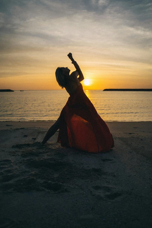 a woman in a red dress is dancing on the beach, pexels contest winner, sun setting, doing a sassy pose, kailee mandel, performing