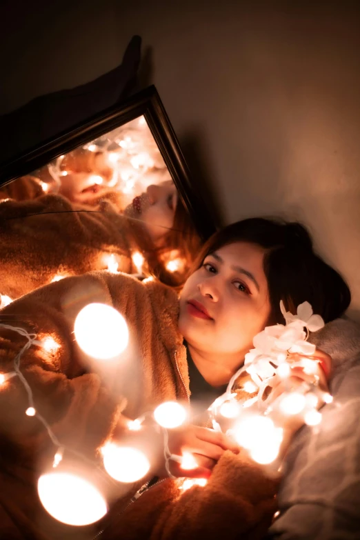 a woman laying on top of a bed next to a mirror, inspired by Elsa Bleda, pexels contest winner, floating lights, an asian woman, lights with bloom, portrait mode photo