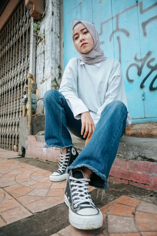 a woman sitting on the ground in front of a building, inspired by Naza, trending on pexels, realism, baggy jeans, portrait full body, cropped wide sleeve, sneaker photo