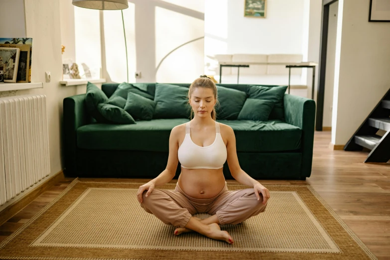 a pregnant woman sitting on a rug in a living room, by Alice Mason, pexels contest winner, health spa and meditation center, physical : tinyest midriff ever, manuka, calm face