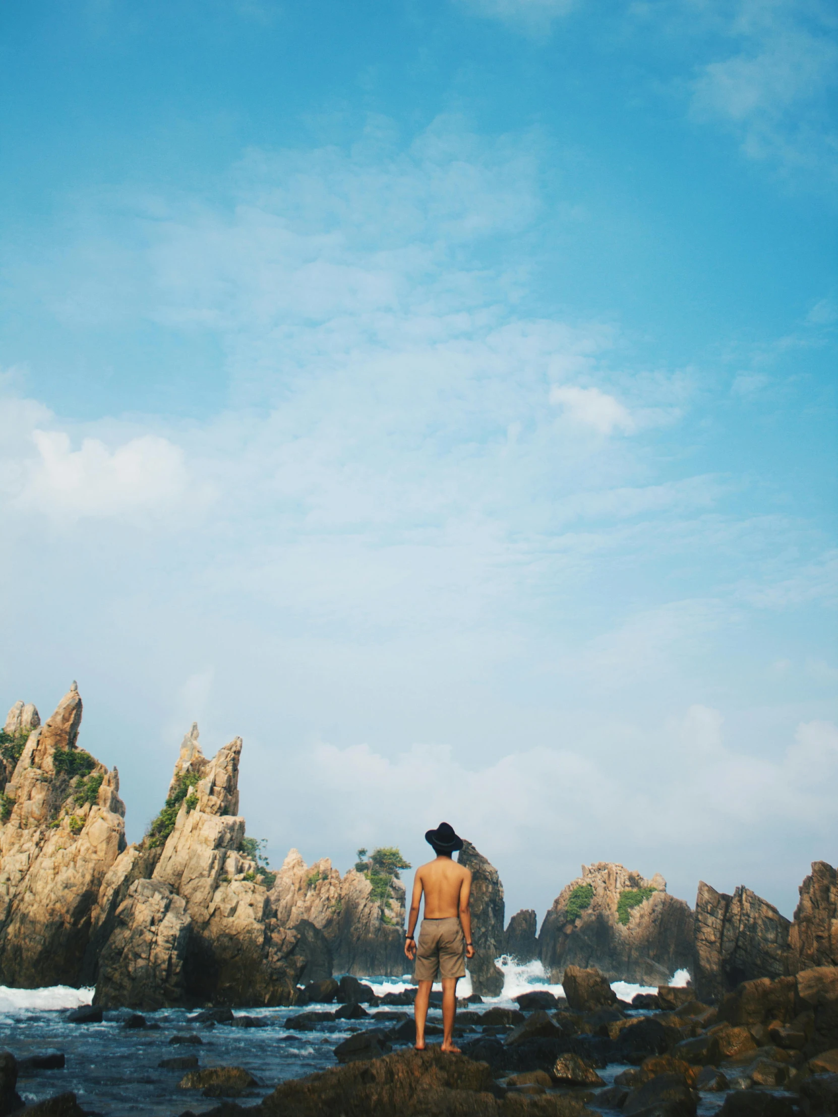 a man standing on top of a rocky beach, by Shen Quan, unsplash, process art, vietnam, tall stone spires, conde nast traveler photo, facing away